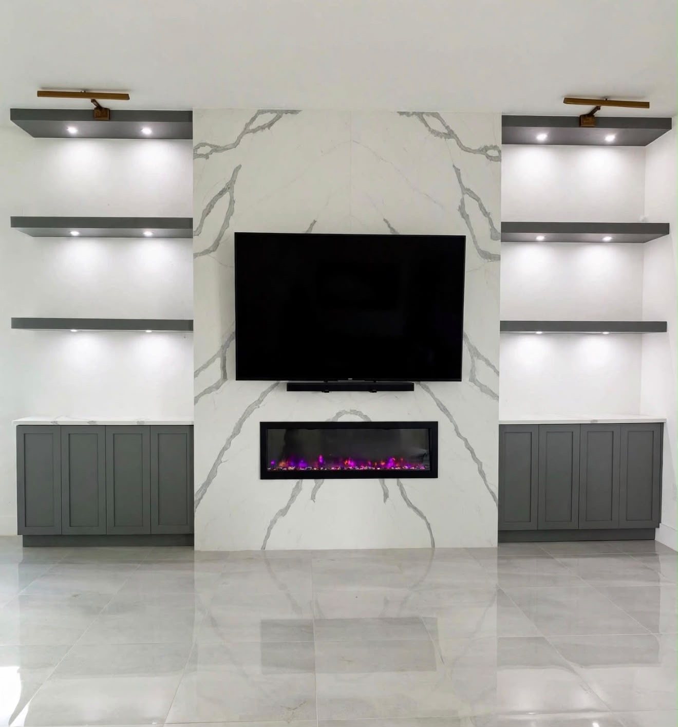 Custom built-in media wall with marble fireplace surround, lighted floating shelves, and gray base cabinets