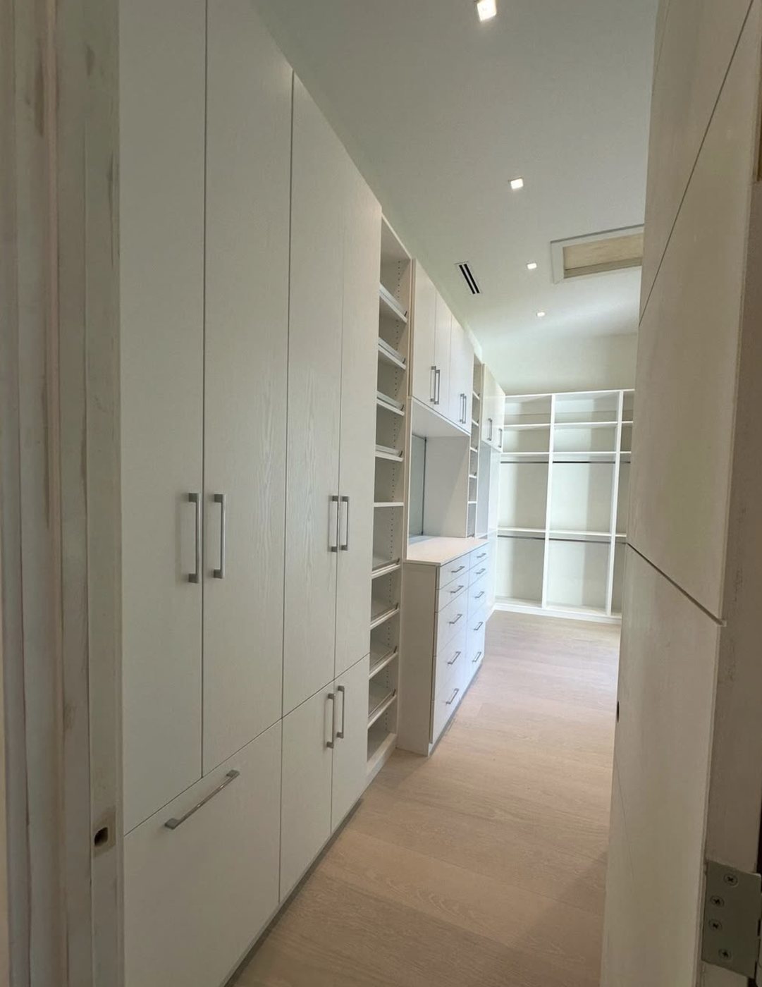 Custom walk-in closet with tall white wardrobe cabinets